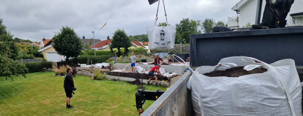 Flaket med storsäck framför en trädgård där folk arbetar