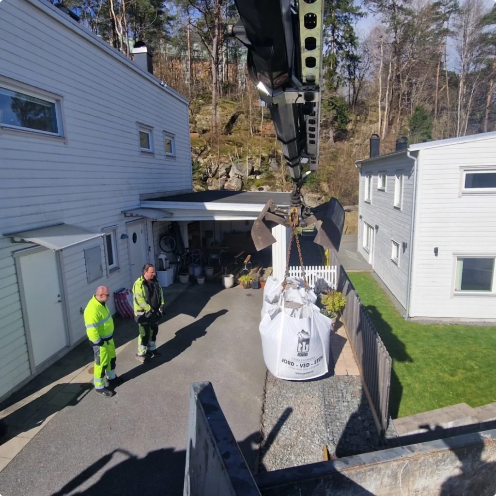 Kranbilen sänker en storsäck grus på en uppfart