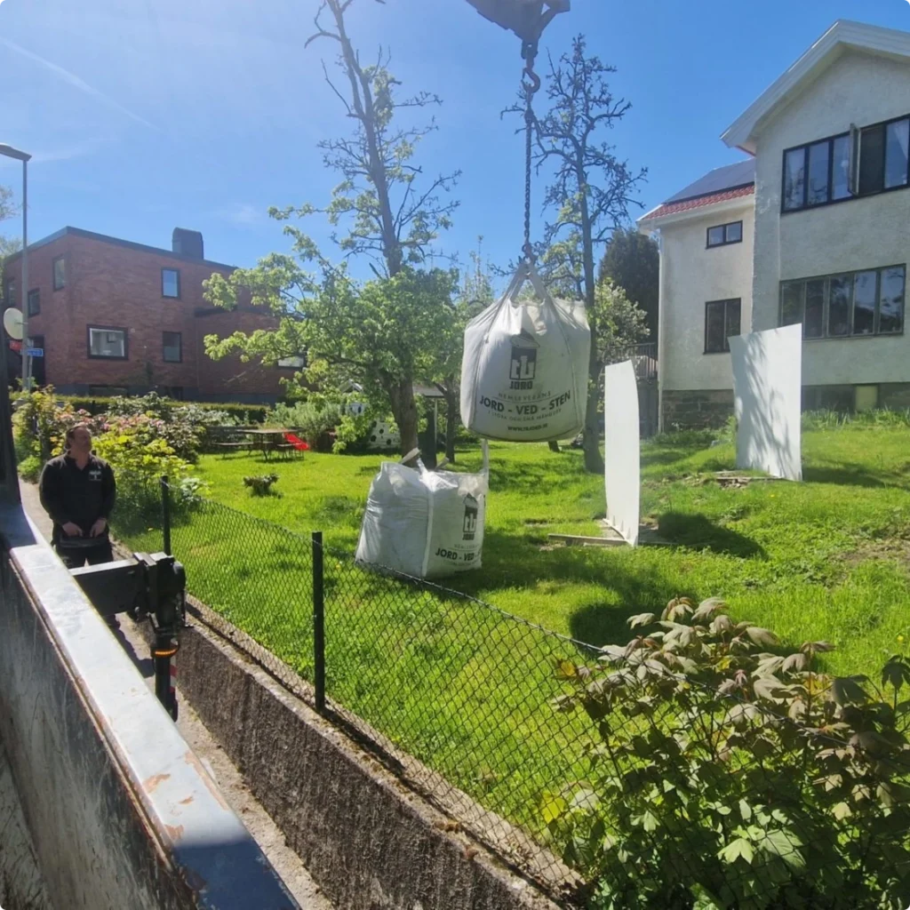 Kranen lyfter en storsäck över staketet in i en villaträdgård