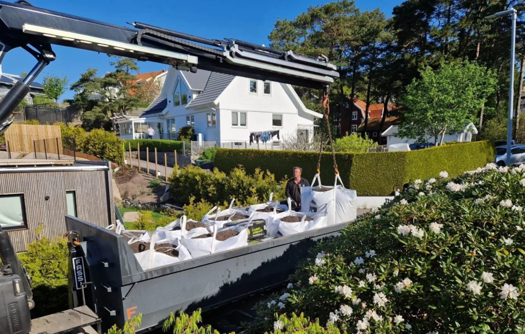 Kranbil från TB Jord med flaket fullt av storsäckar jord utanför en villa i Göteborg
